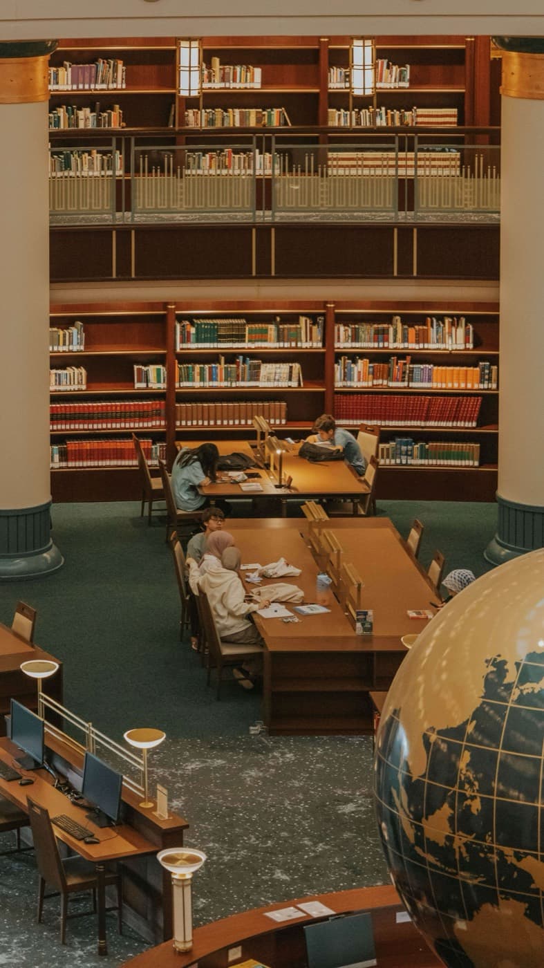 Students working at long tables in a reading room lined with bookcases