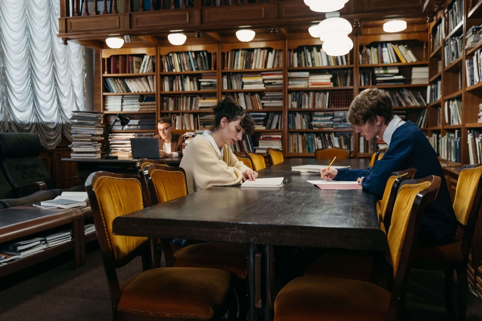 Students working through coursework at a long library reading table