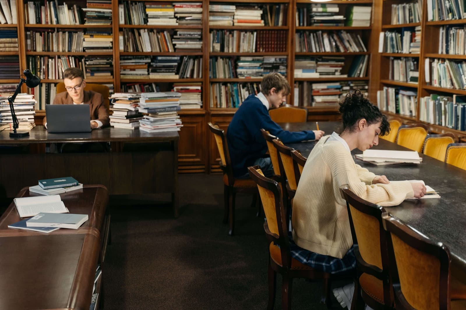 Students working through stacks of books and printouts at a library desk