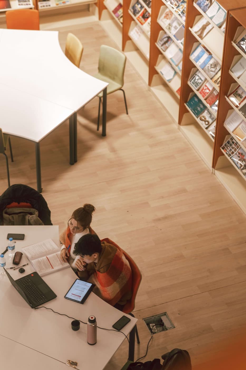 Students working with laptops at a library desk, seen from above